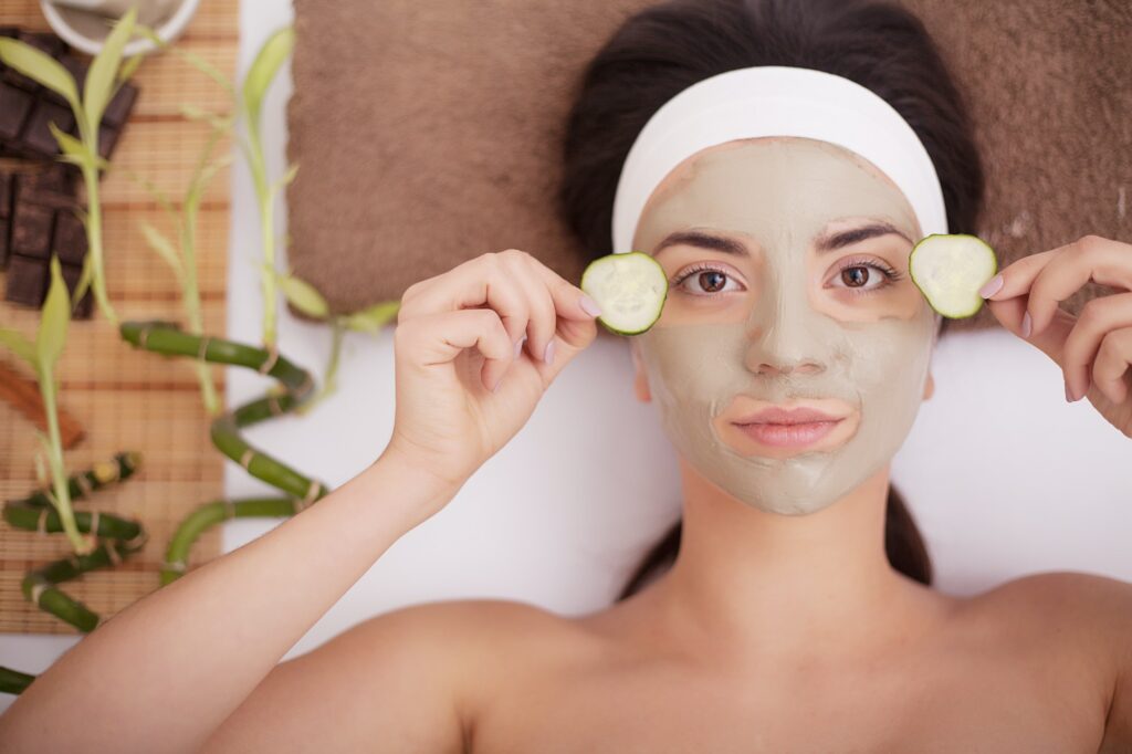 Woman with clay facial mask in beauty spa. In background tropical plants